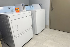 Un lavadero con dos lavadoras y secadoras apiladas, una caja de detergente Tide y una puerta.