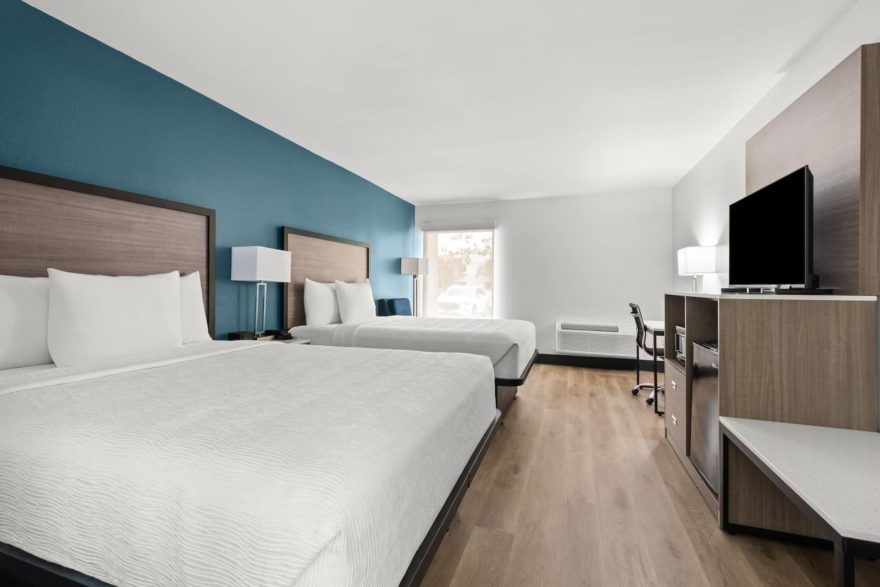 A hotel room with two beds, a desk, a chair, a television, and a window.