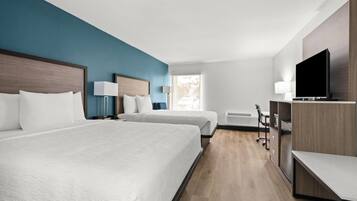 A hotel room with two beds, a desk, a chair, a television, and a window.
