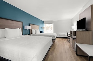 Una habitación de hotel con dos camas, un escritorio, una silla, un televisor y una ventana.
