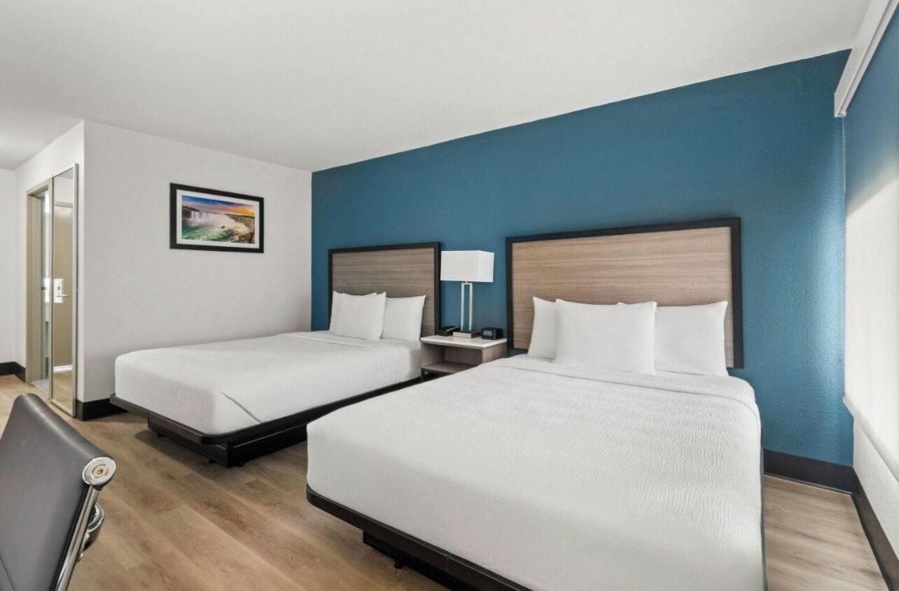 Een hotelkamer met twee bedden, een nachtkastje, een lamp en een schilderij aan de muur.