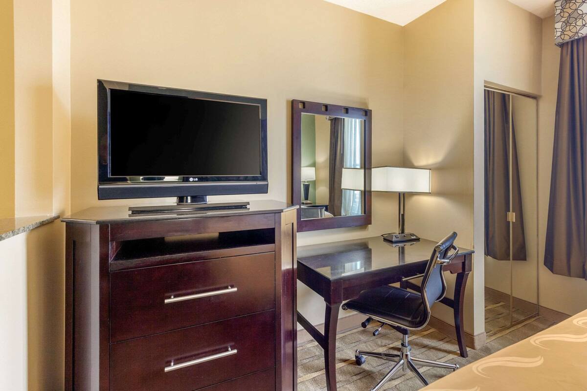 A hotel room with a desk, chair, TV, and a mirror.