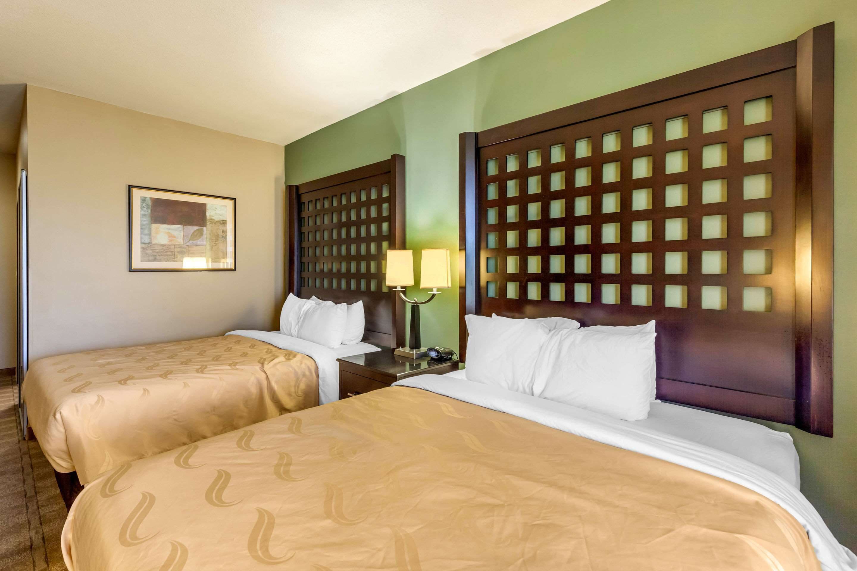 A hotel room with two beds, a nightstand with a lamp, and a framed picture on the wall.