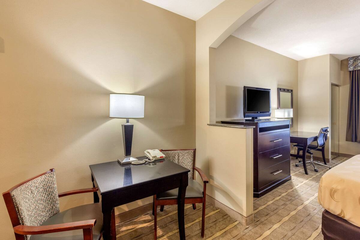 A hotel room with a desk, chair, bed, dresser, TV, and mirror.