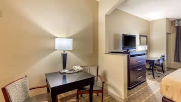 Habitación de hotel con escritorio, silla, cama, cómoda, televisión y espejo.