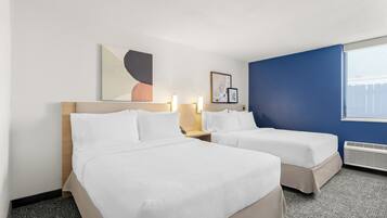 A hotel room with two beds, a large window, and artwork on the wall.