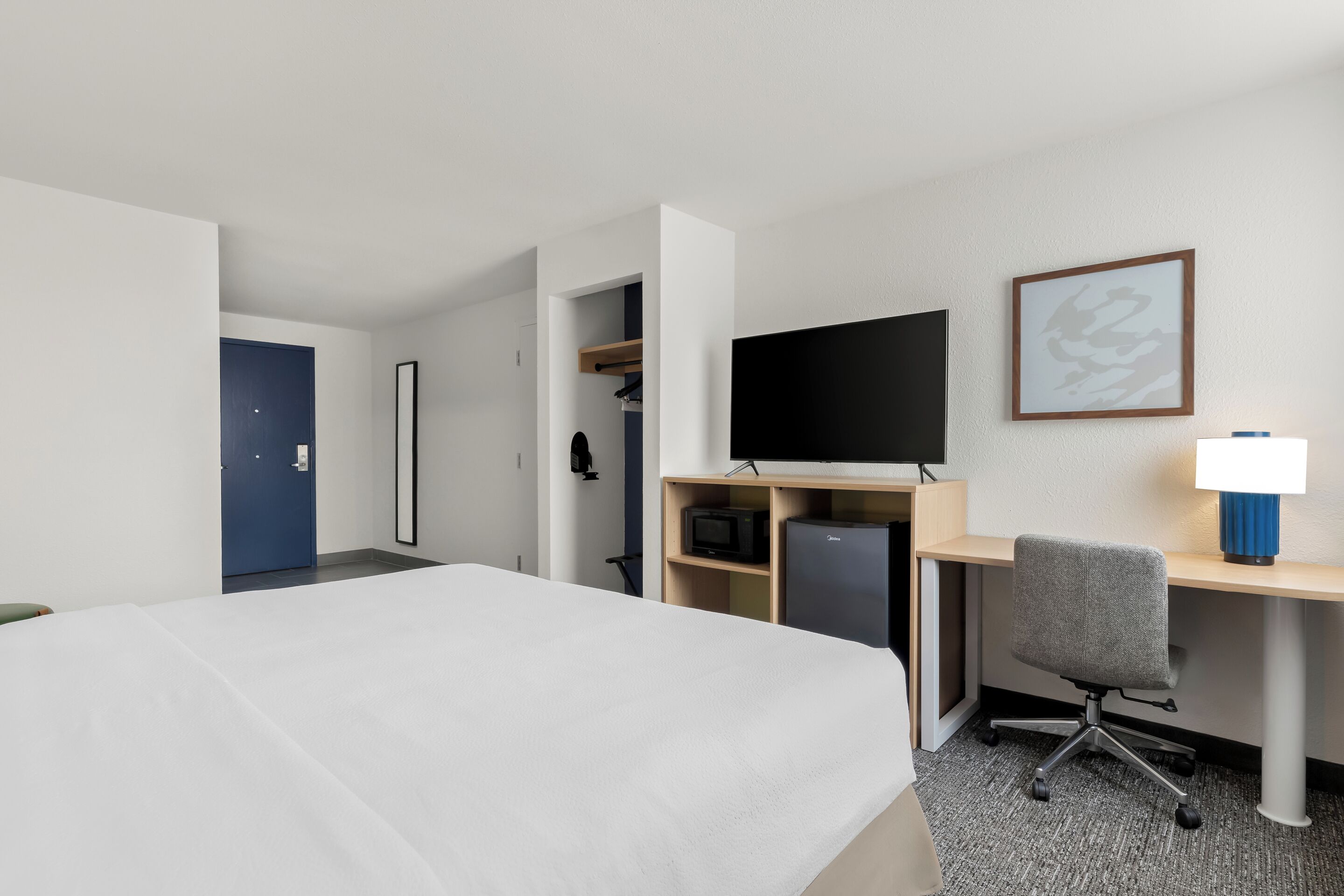 Habitación de hotel con una cama, un escritorio con computadora, un televisor y una lámpara.