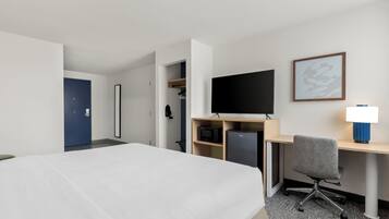 Habitación de hotel con una cama, un escritorio con computadora, un televisor y una lámpara.