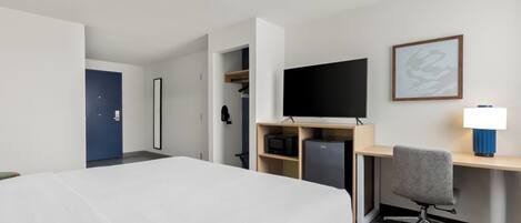 A hotel room with a bed, a desk with a computer, a TV, and a lamp.