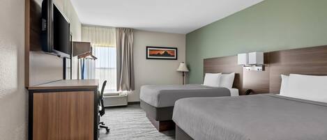 Habitación de hotel con dos camas, un escritorio con televisor, una lámpara y una ventana con cortinas.