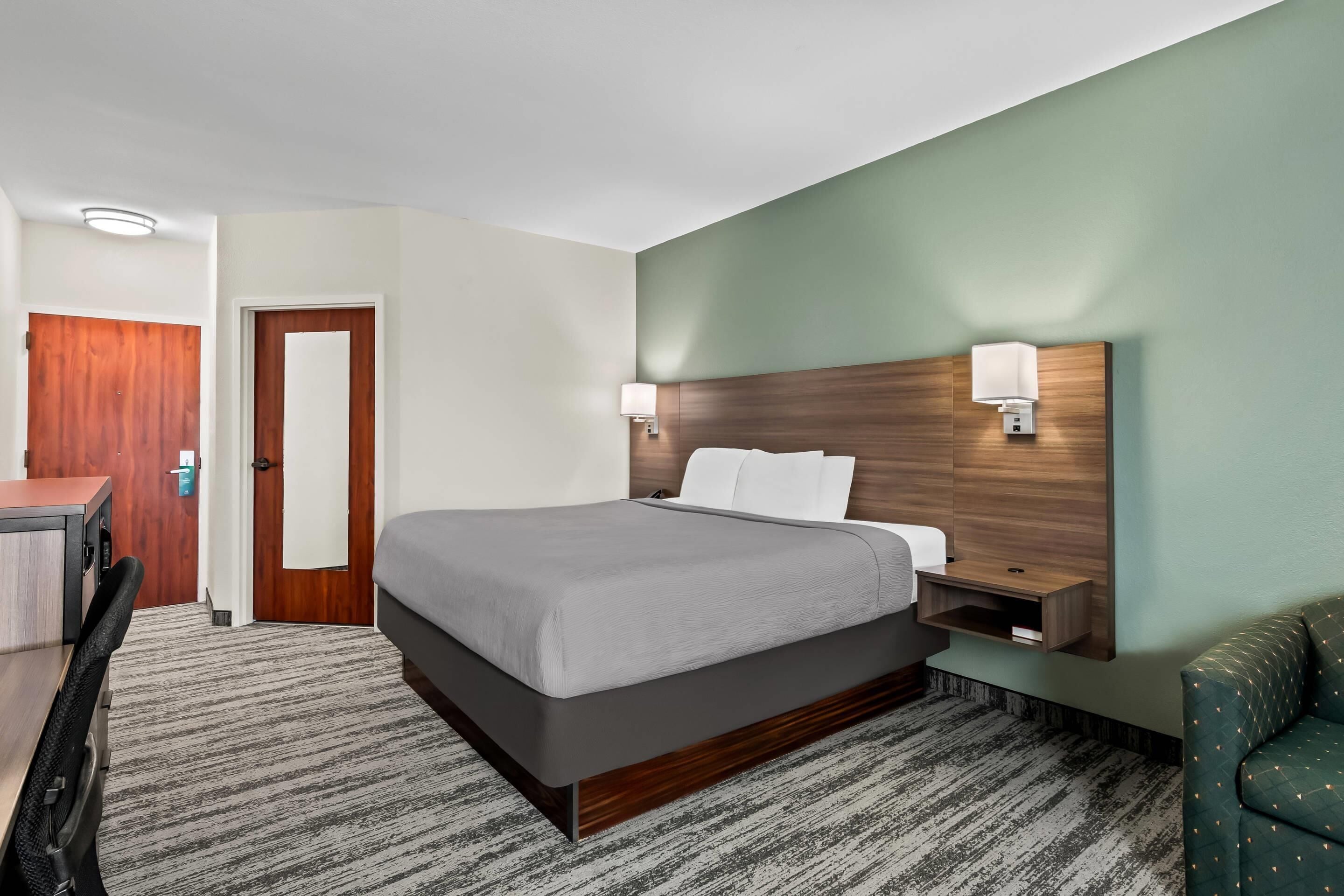 A hotel room with a bed, bedside tables, a desk, and a chair.
