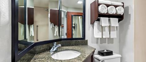 Une salle de bain avec un lavabo doté d’un plan de travail en granit, un grand miroir, un porte-serviettes avec des serviettes pliées et des toilettes.