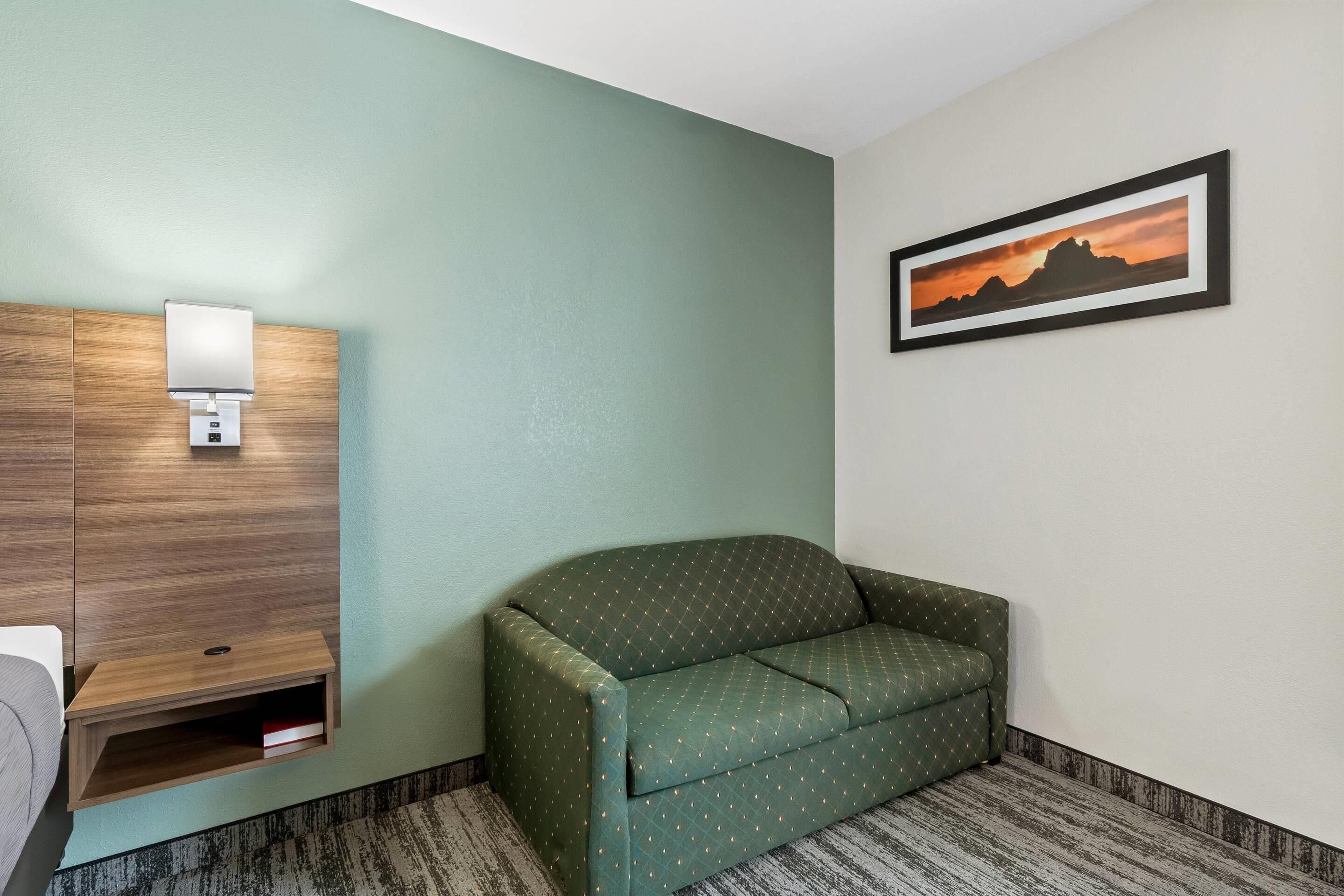 A room with a green sofa, a wooden cabinet with a light, and a framed picture on the wall.