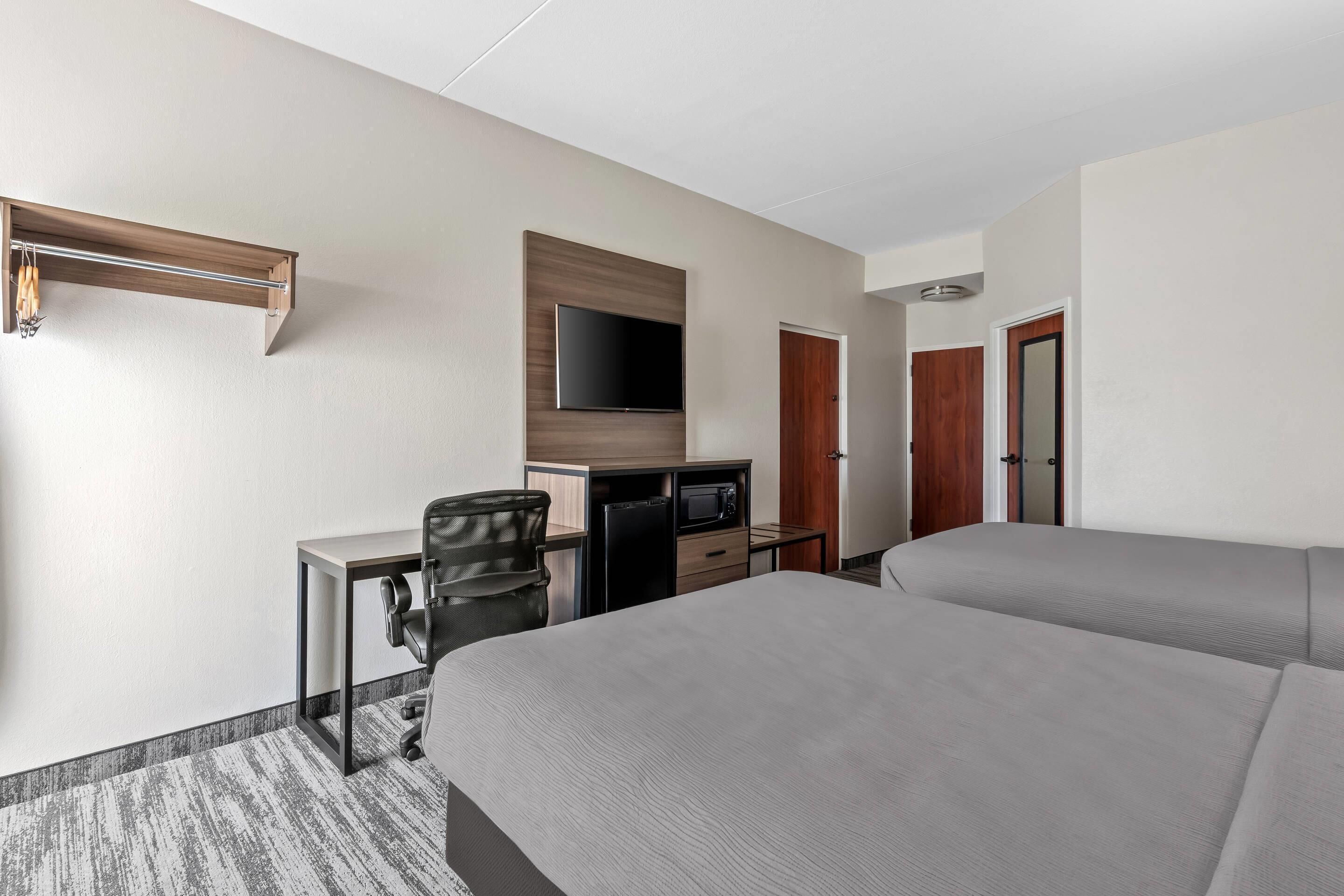 Habitación de hotel con dos camas, un escritorio con silla, televisor montado en la pared y un microondas.