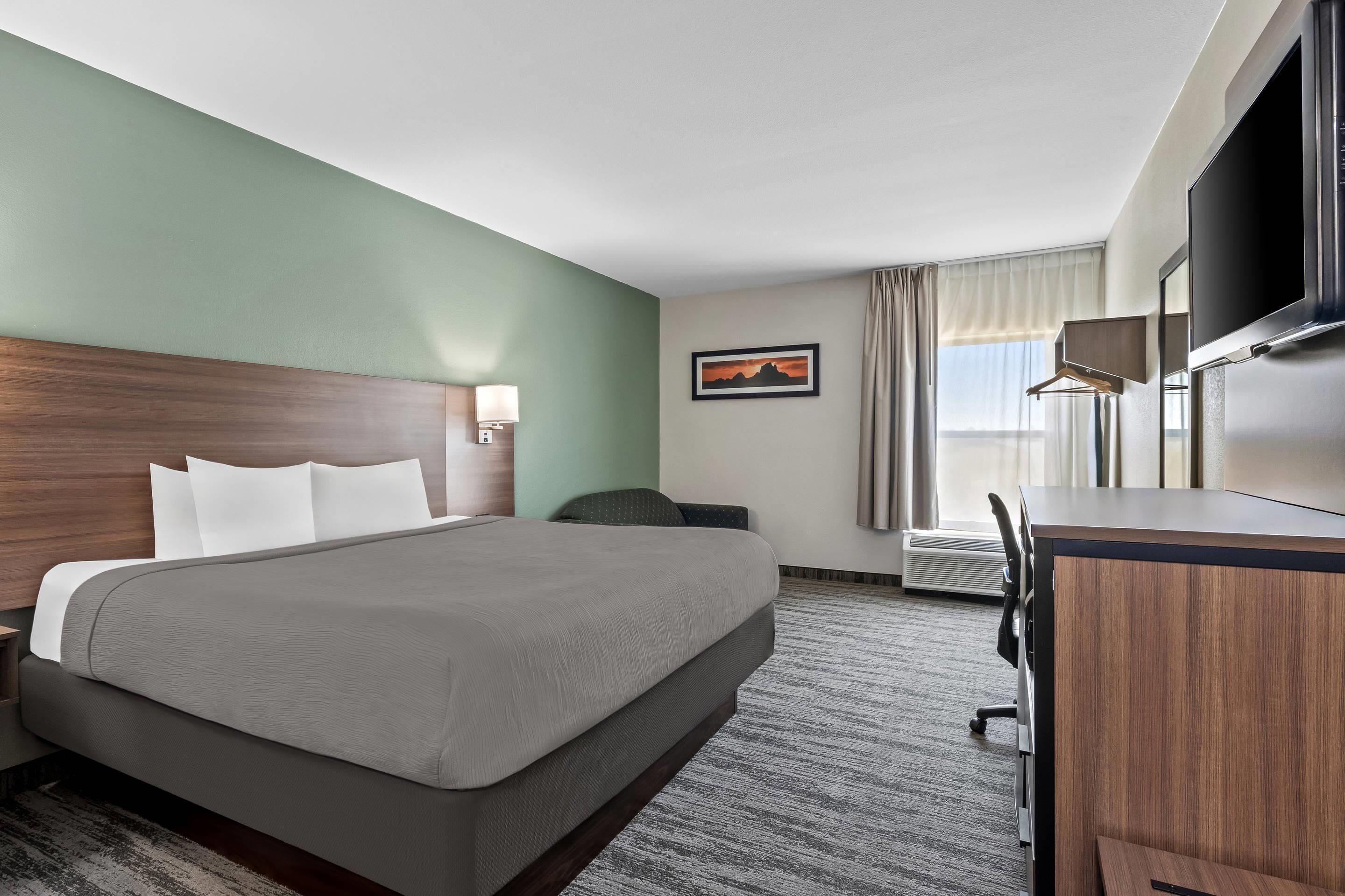 A hotel room with a large bed, a desk, a chair, a TV, and a window with curtains.