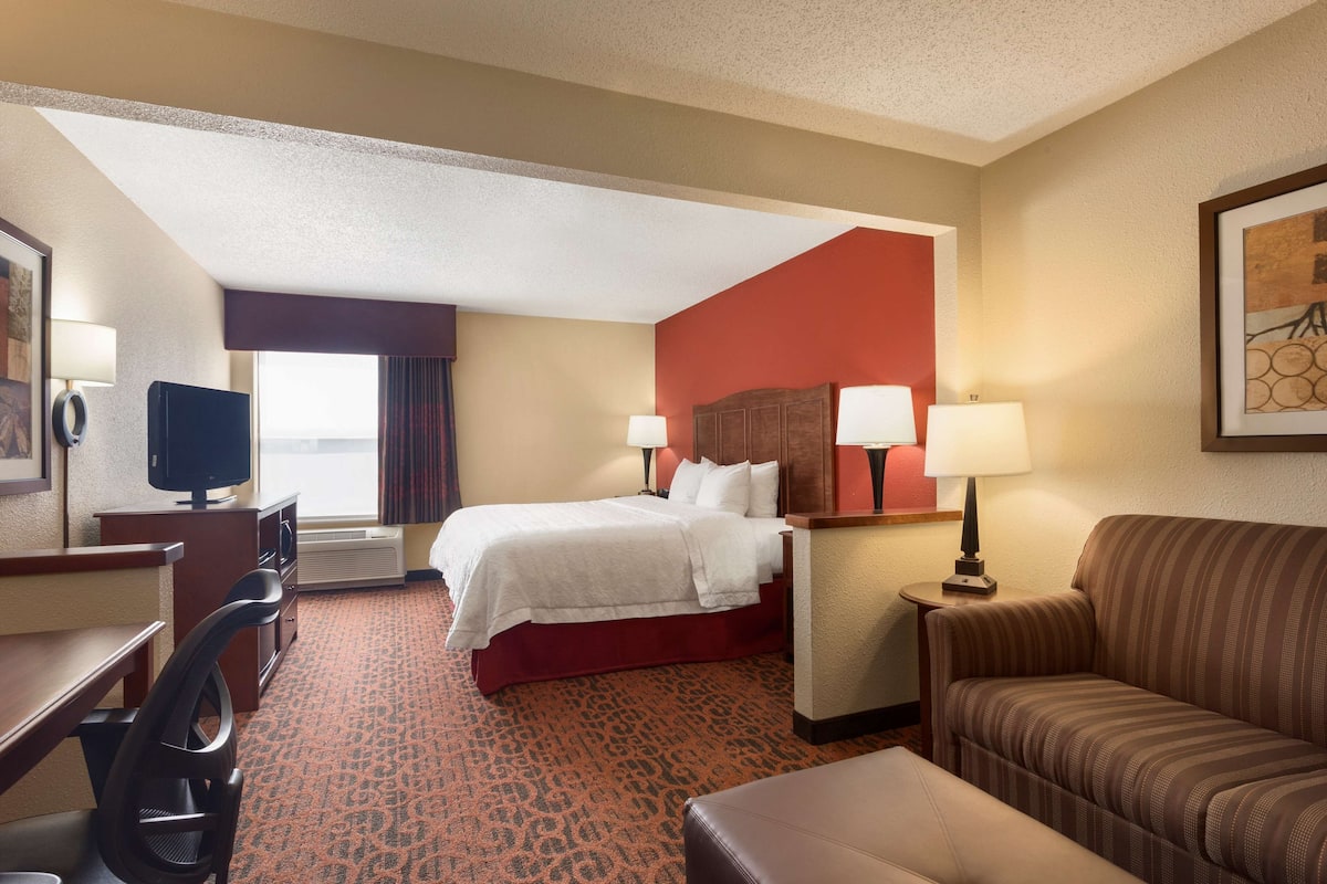 A hotel room with a bed, a desk, a chair, a sofa, and a TV.