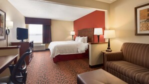 A hotel room with a bed, a desk, a chair, a sofa, and a TV.