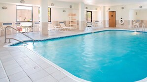 A large indoor swimming pool with clear blue water, surrounded by white lounge chairs and a tiled floor.