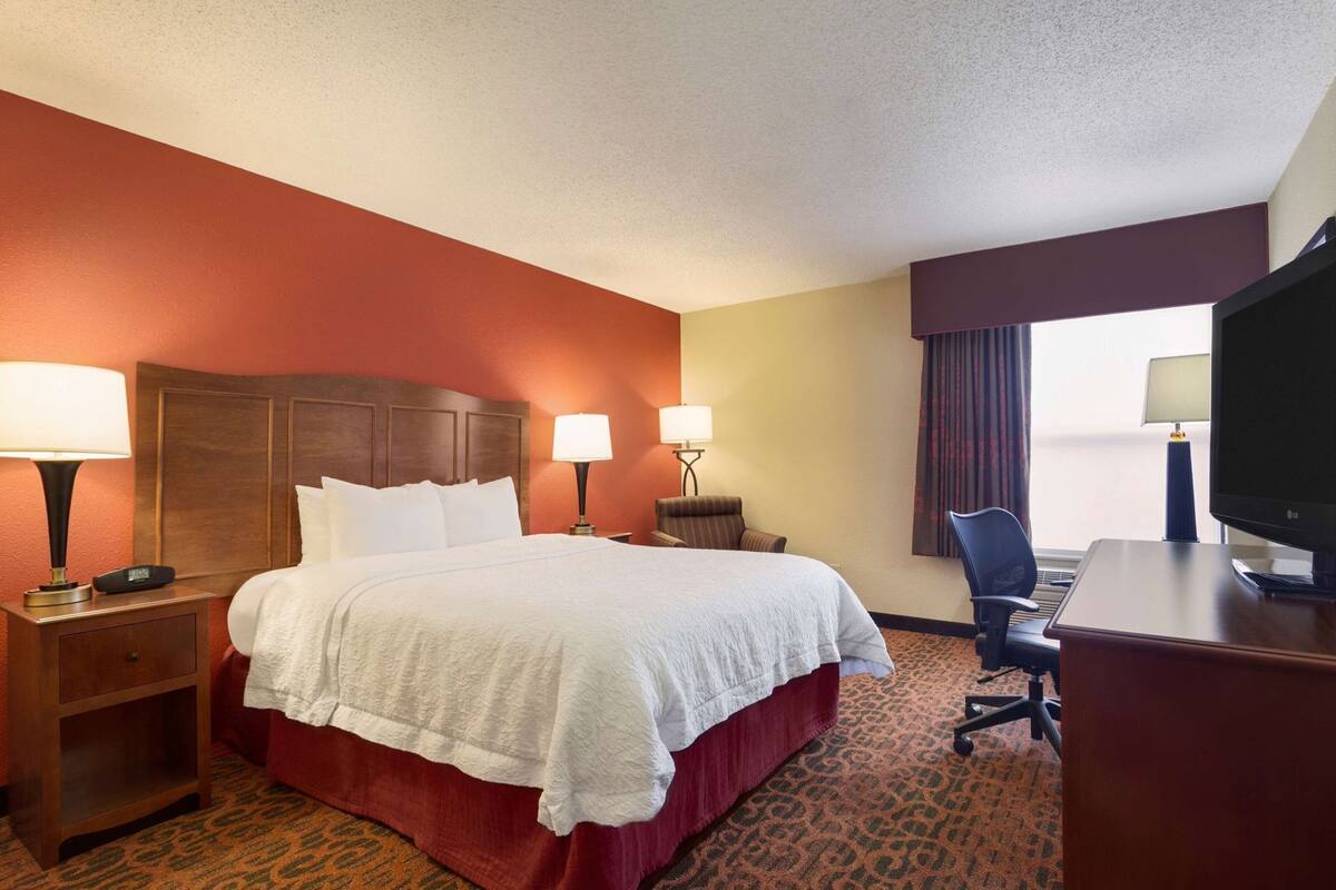 A hotel room with a large bed, two bedside tables with lamps, a desk with a chair, and a television.