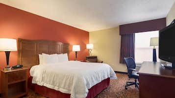 A hotel room with a large bed, two bedside lamps, a desk with a chair, and a television.