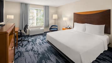 Quarto de hotel com uma cama grande, uma escrivaninha, uma cadeira, televisão e janela com cortinas.
