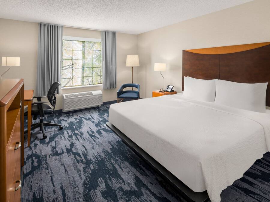 Quarto de hotel com uma cama grande, uma escrivaninha, uma cadeira, televisão e janela com cortinas.