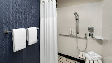 A bathroom with a shower, a towel rack with towels, a toilet, and a sink with toiletries.