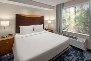 Habitación de hotel con una cama grande, una mesita de noche con una lámpara, un teléfono y una ventana con vistas a árboles.