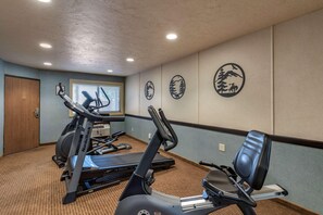 A gym with treadmills and stationary bikes, a wooden door, and a window with blinds. - Quality Inn Madras (Madras)