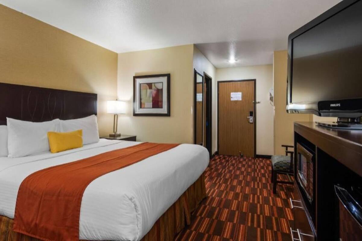 Quarto de hotel com uma cama, televisão, escrivaninha e porta.