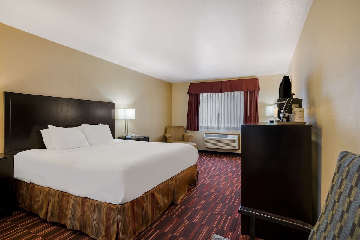 Quarto de hotel com uma cama grande, uma escrivaninha com abajur, uma cadeira, ar condicionado e uma televisão.
