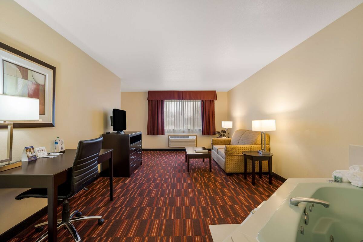 Quarto de hotel com escrivaninha, cadeira de escritório, sofá e uma banheira grande.