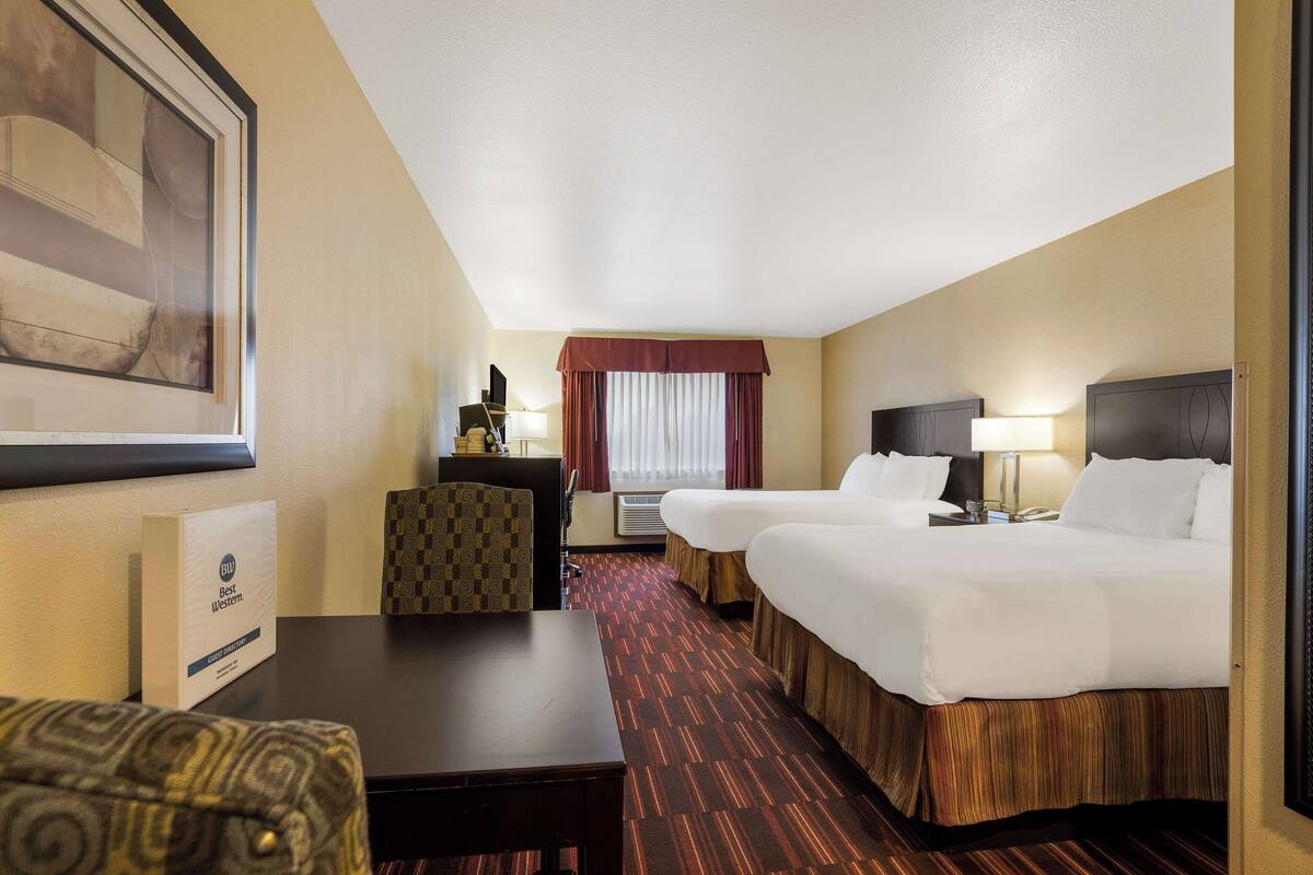 Quarto de hotel com duas camas, uma escrivaninha, uma cadeira, uma televisão e uma janela com cortinas.