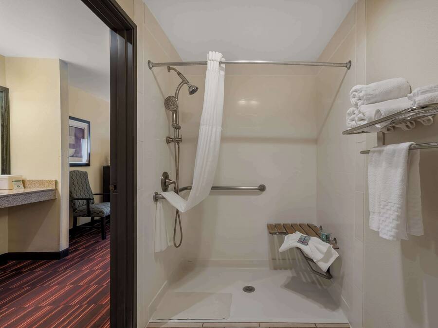 Un área de ducha moderna con puerta de cristal, un perchero con toallas dobladas y un banco de madera.