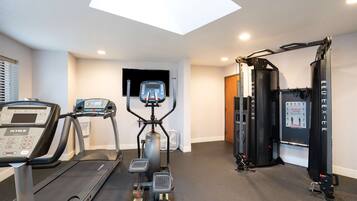Gimnasio en casa con cinta de correr, elíptica y equipo de levantamiento de pesas.