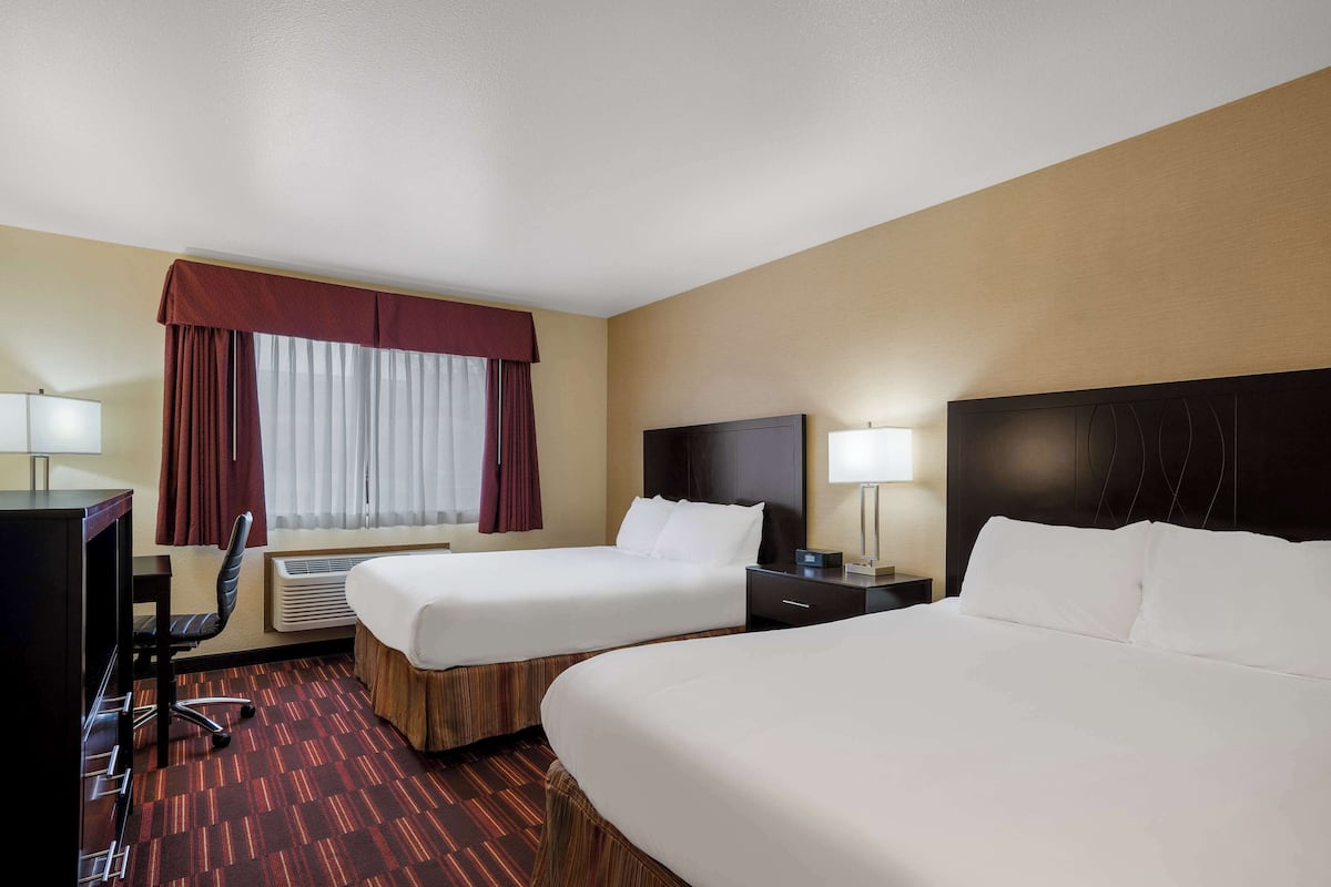 Quarto de hotel com duas camas, uma escrivaninha, uma cadeira, uma televisão e uma janela com cortinas.