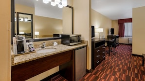 A hotel room with a kitchenette, a large mirror, a coffee maker, a microwave, a refrigerator, a desk with a chair, and a window with curtains. - Best Western Hermiston Inn (Hermiston)