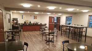 A spacious indoor area with multiple tables and chairs, a counter with various items, and an exit sign. - Best Western Sandy Inn (Sandy)