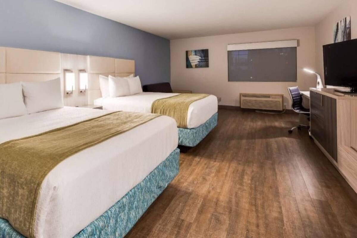 A hotel room with two beds, a desk, a television, and a window.