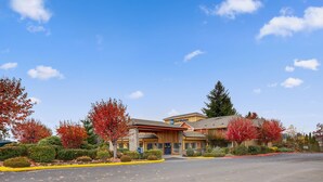 A hotel with a central entrance, surrounded by autumn foliage, a parking lot, and a clear blue sky. - Best Western Sandy Inn (Sandy)