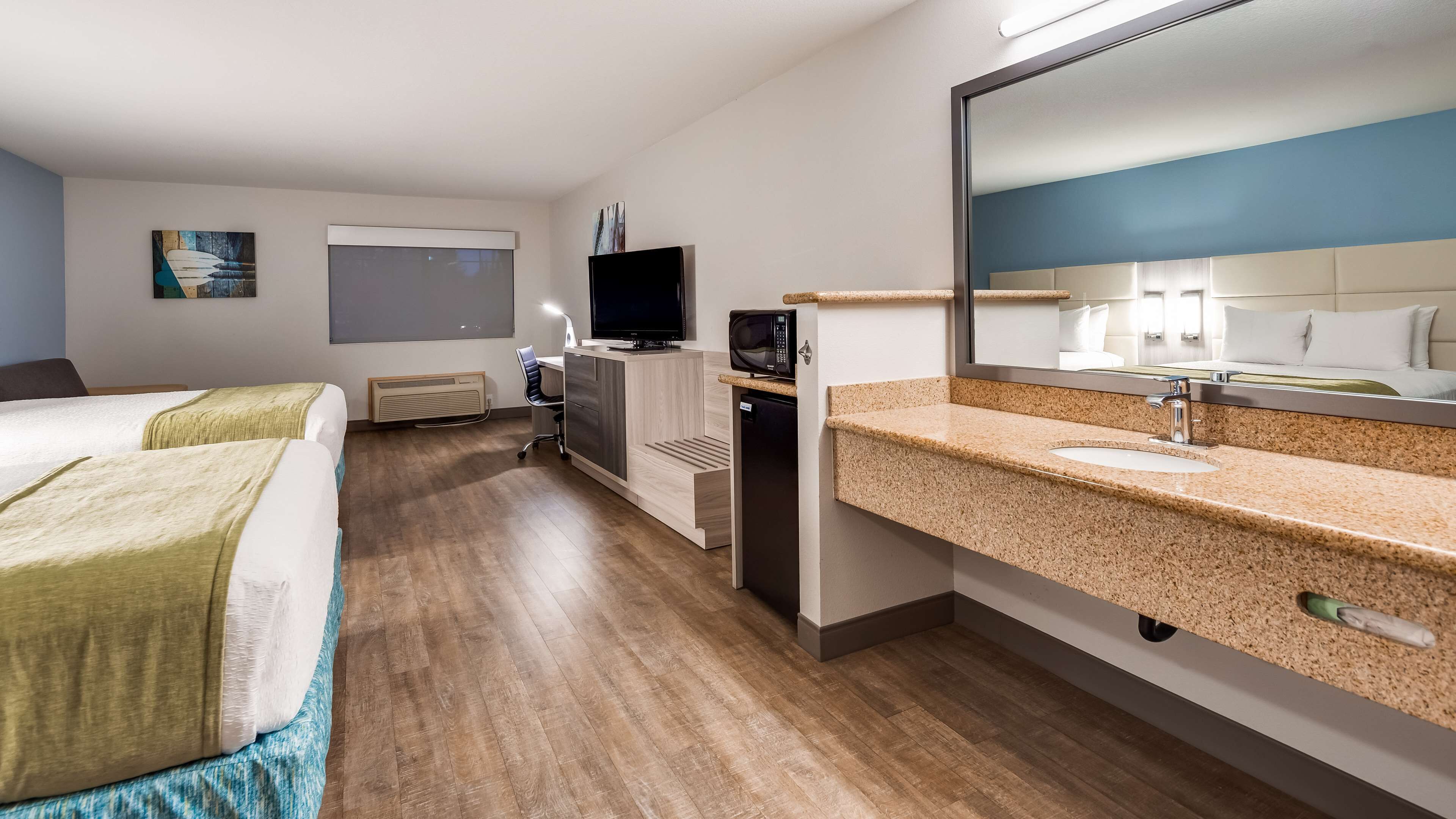 A hotel room with two beds, a TV, a microwave, a desk, and a large mirror.