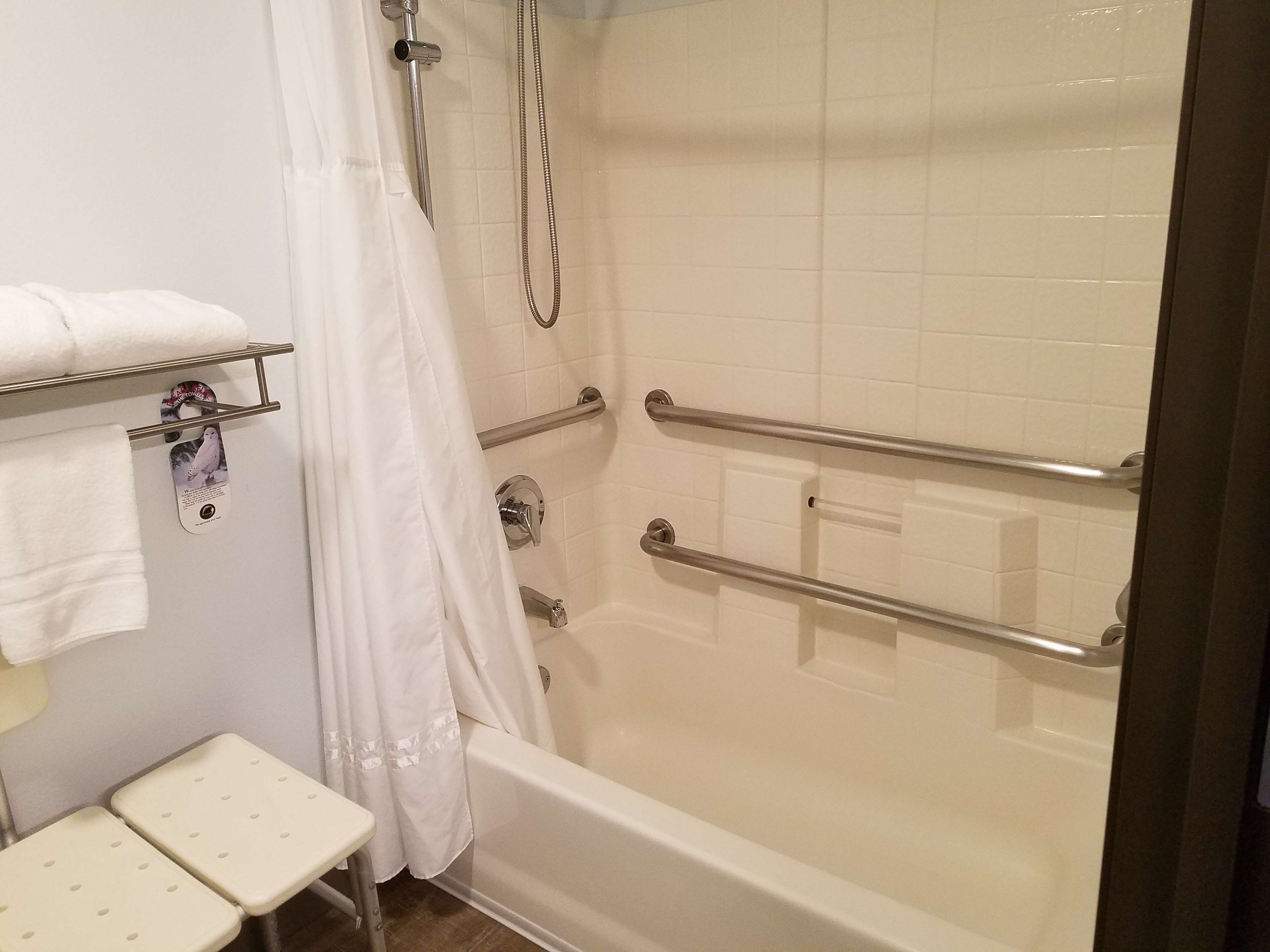 Badeværelse med badekar, bruser og toilet. Der er installeret gelænder for sikkerhedens skyld.