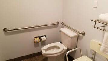 A small bathroom with a toilet, grab bars, a towel rack, and a toilet paper holder.