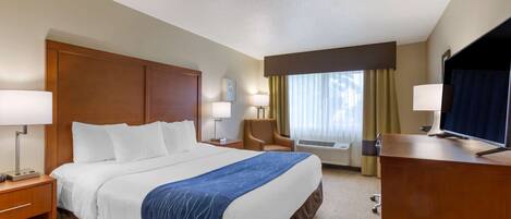 A hotel room with a large bed, two bedside tables with lamps, a desk with a television, and a chair.