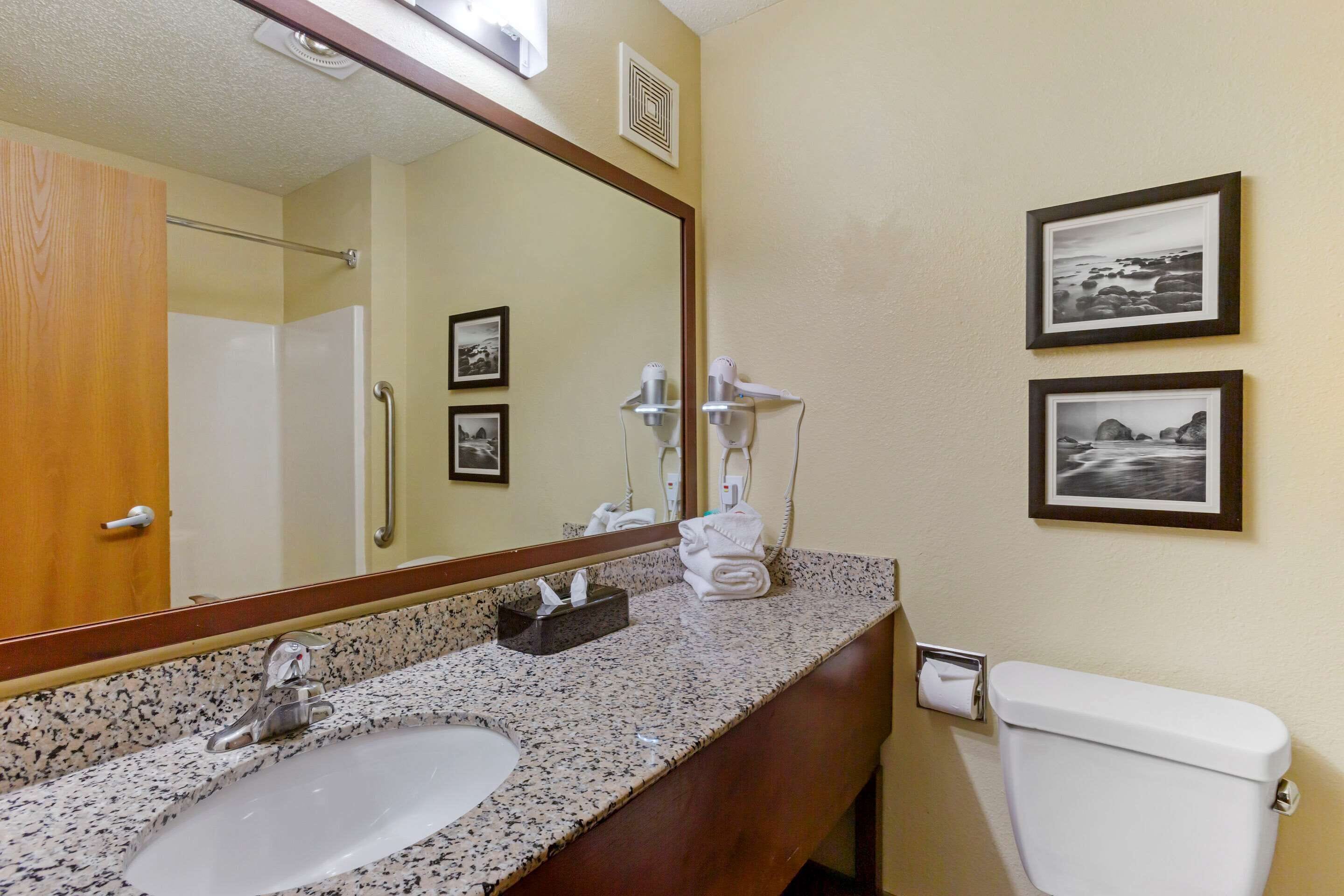 A bathroom with two sinks, a mirror, a toilet, and two framed pictures on the wall.