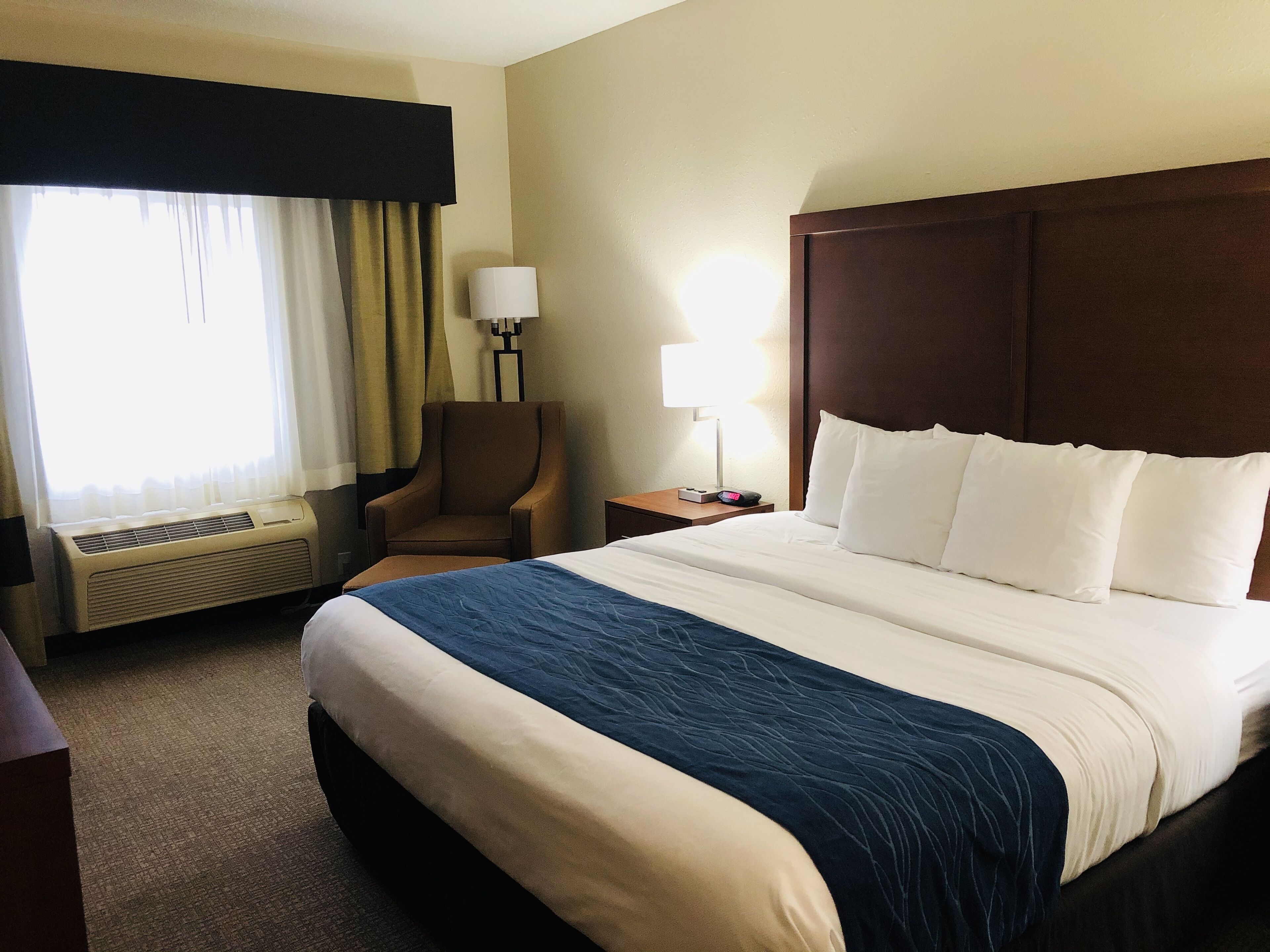 Una habitación de hotel con una cama grande, una silla, un escritorio, una lámpara y una ventana con cortinas.