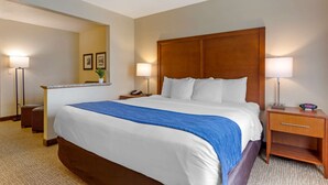 Habitación de hotel con una cama grande, dos mesitas de noche, un tocador, un espejo y una lámpara de pared.