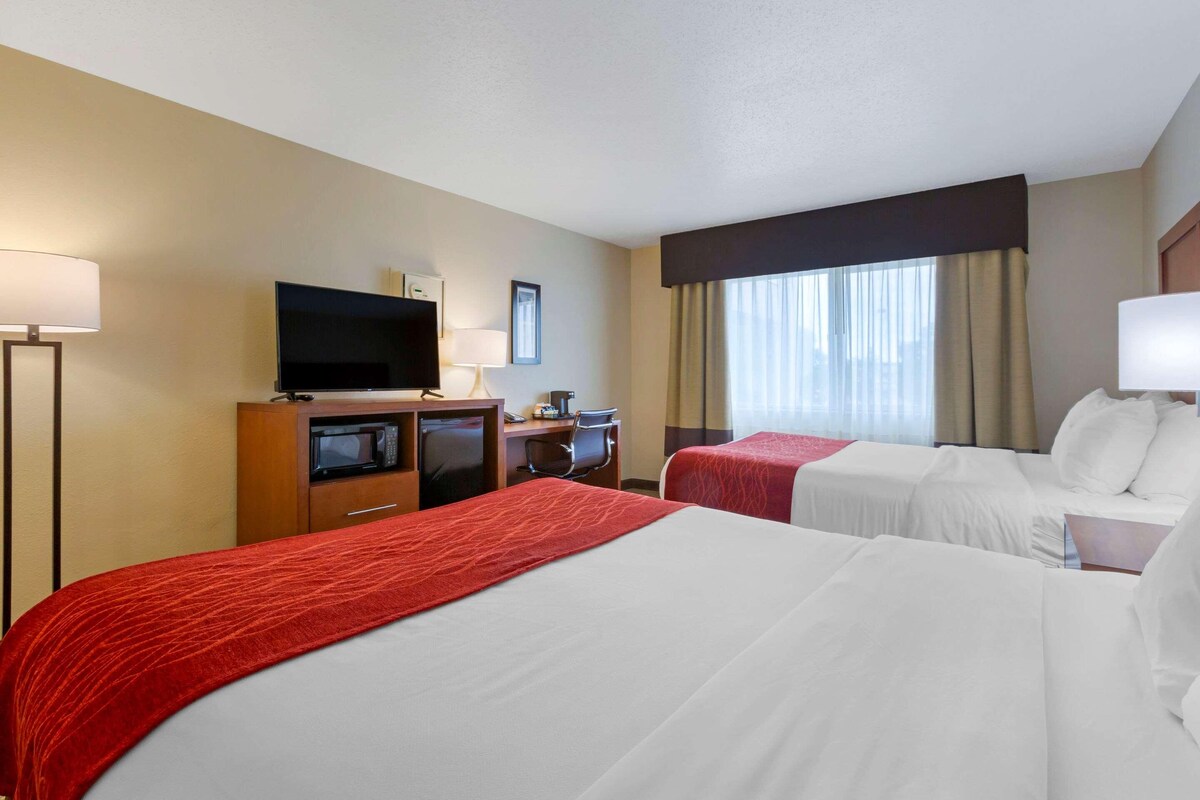 A hotel room with two beds, a TV, a desk with a computer, and a window with curtains.