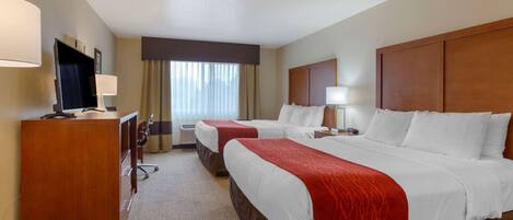 A hotel room with two beds, a desk with a TV, a desk lamp, and a window with curtains.