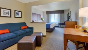 Una habitación de hotel con un sofá azul, una mesa de madera, una cama con cubrecama azul y blanco, un escritorio con lámpara y dos cuadros en la pared.